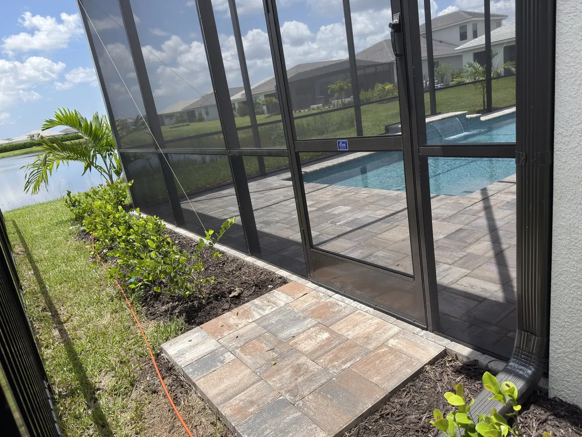 Screen door and side wall of a bronze pool cage beside a paver walkway, Bradenton area job