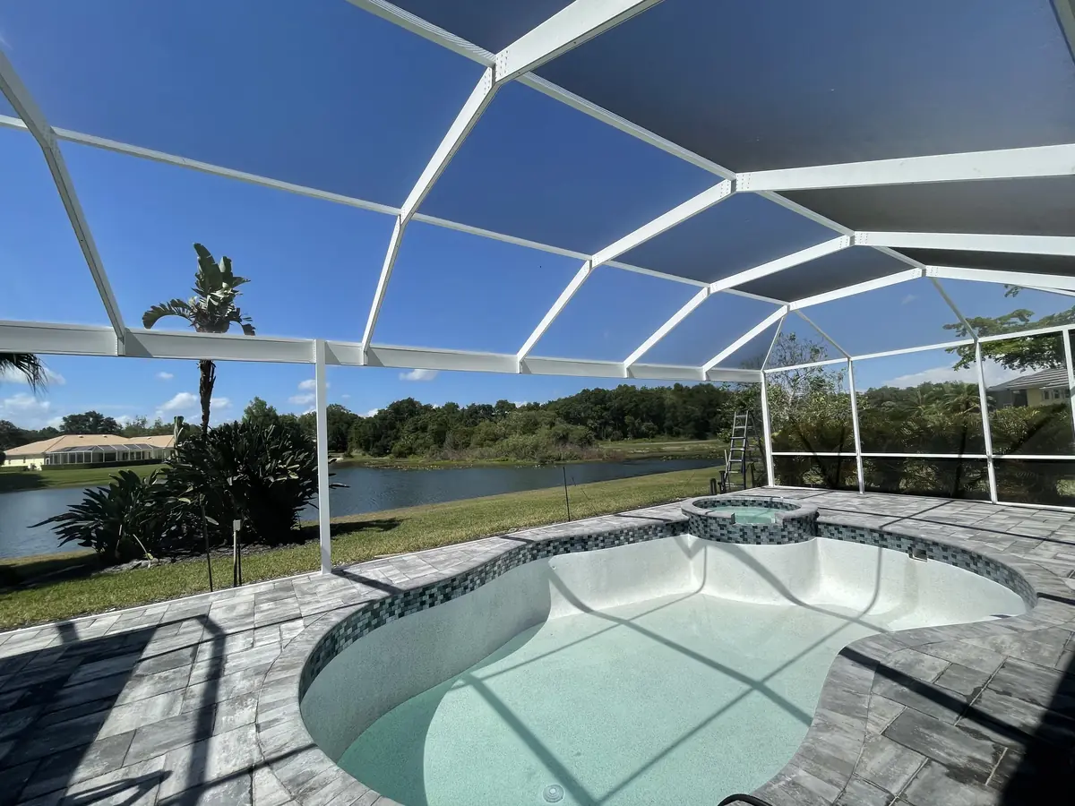 White frame pool enclosure over a pool and spa with a paver deck and lake view
